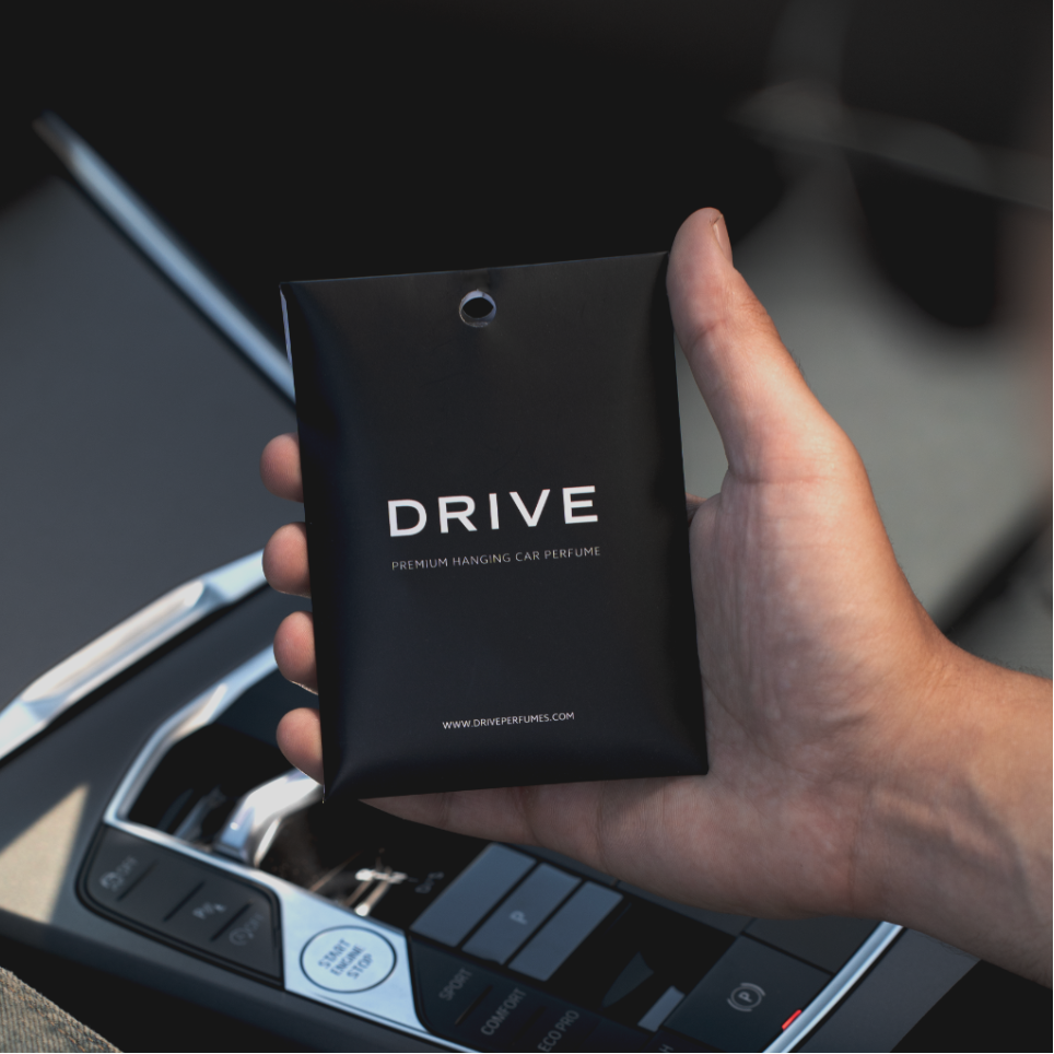 Hand holding a black 'Drive' car perfume packaging inside a vehicle.
