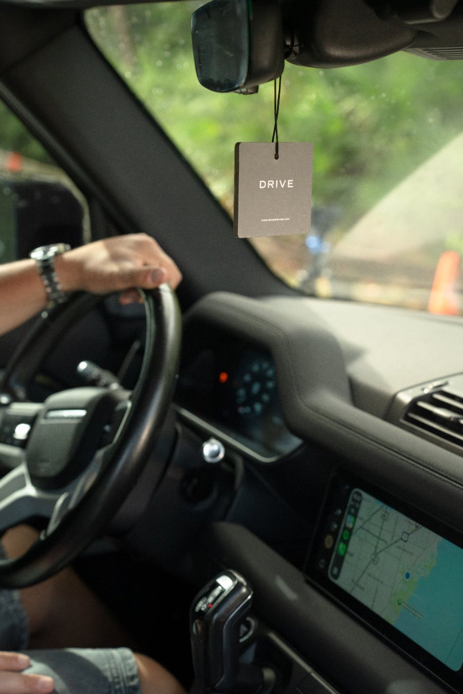 Driver at the wheel with a Drive hanging car perfume card on the rearview mirror
